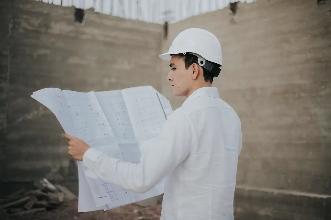 Architect in a hard hat reading a large blueprint on site