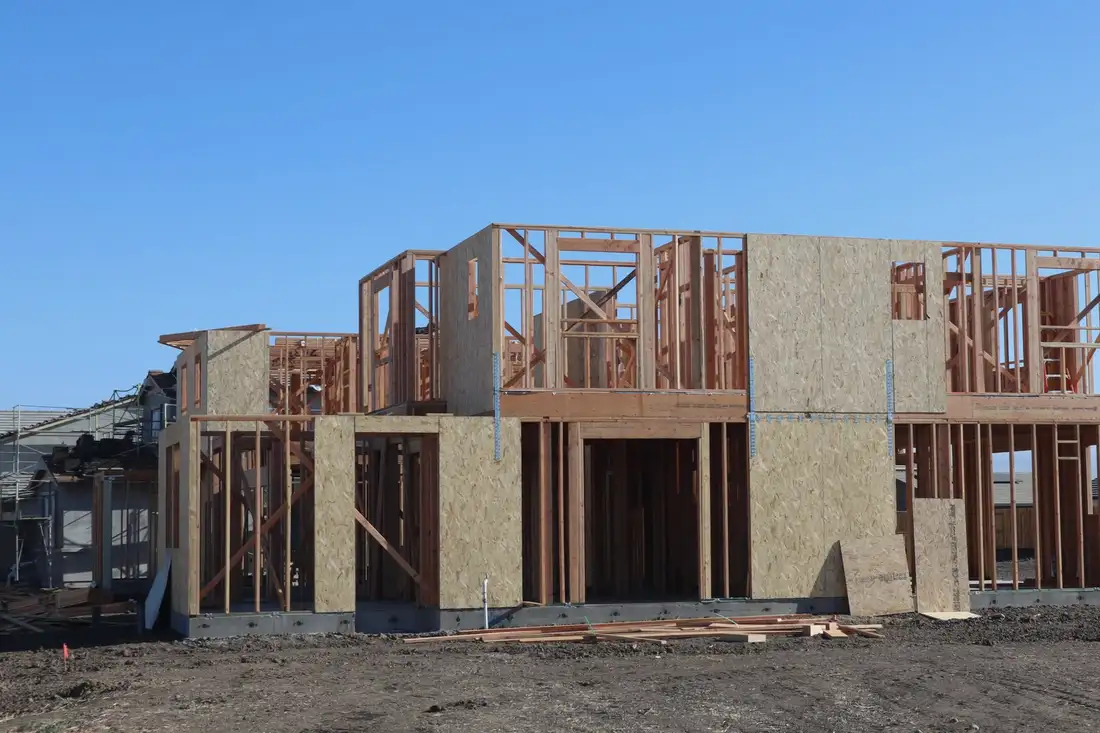 Timber wall framing standing on a new foundation under a blue sky