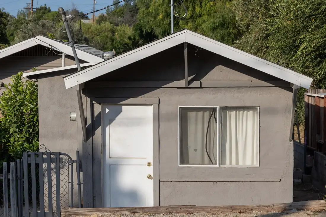 Small grey detached garage building with a door and window