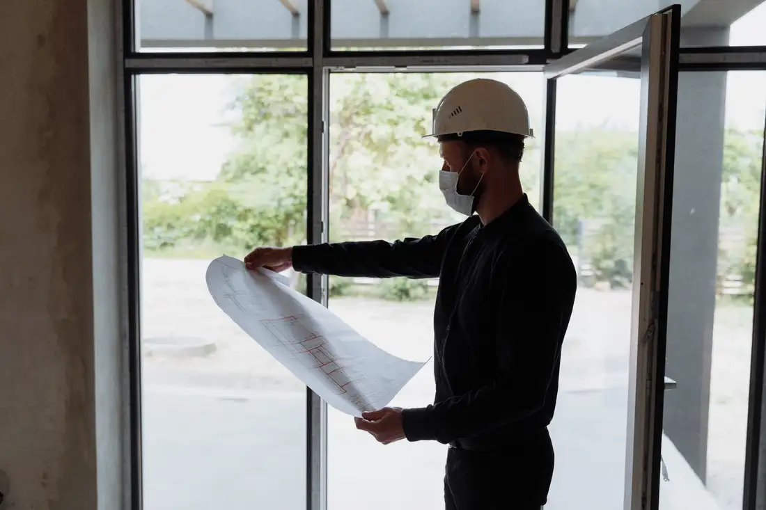 Builder holding open a floor plan against a bright window
